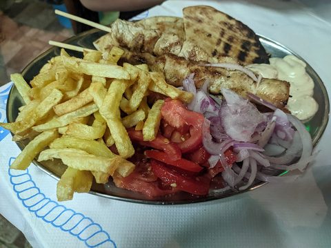 Representative photograph of Chicken Souvlaki. The photograph includes chips, bread, salad and sauce not included in this draft.