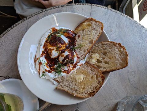 Representative photograph of Cilbir. Toast and herbs are shown alongside the eggs and yogurt.