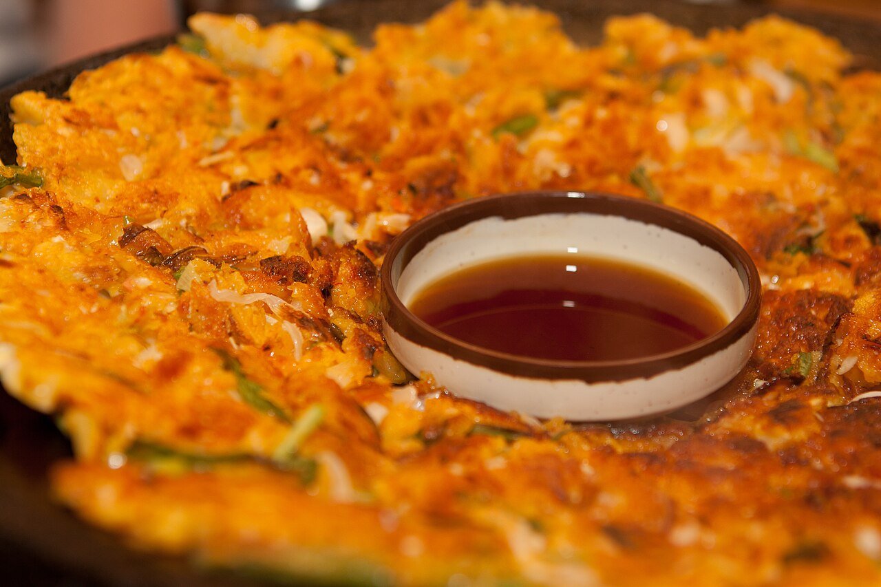 Representative photograph of Haemul Pajeon. The photograph includes a dipping sauce presented in the centre of the pancake.