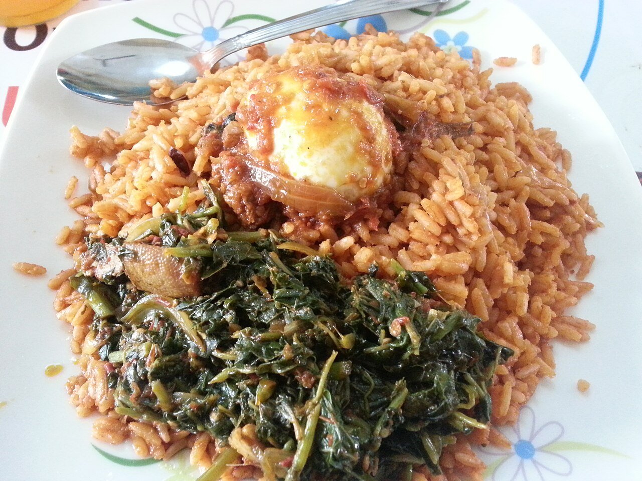 Representative photograph of Jollof Rice. The photograph includes egg and a cooked greens side; this draft makes only the jollof rice.