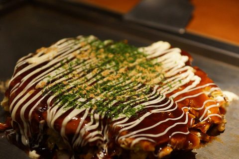 Representative photograph of Okonomiyaki. The photograph includes extra green garnish not included in the draft.
