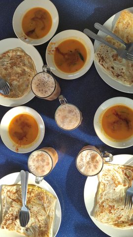 Representative photograph of Roti Canai. The photograph shows a breakfast spread with curry and drinks; this draft makes the roti only.