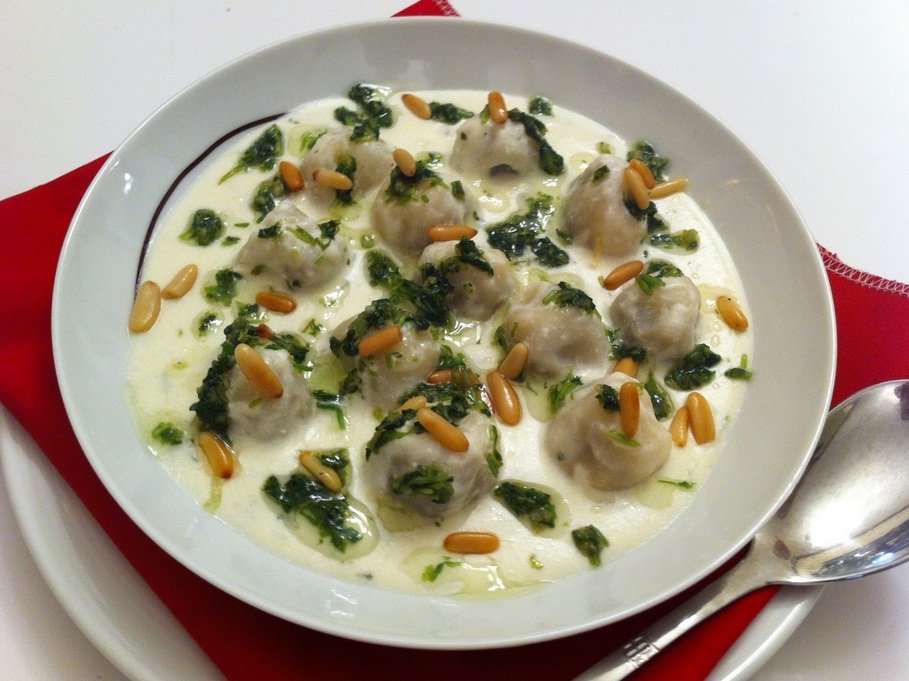 Representative photograph of Shish Barak. The photograph includes a herb and nut garnish.
