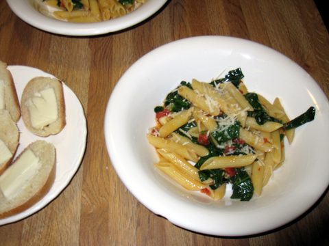 Photograph of penne with spinach, tomatoes and grated Parmesan on a white plate